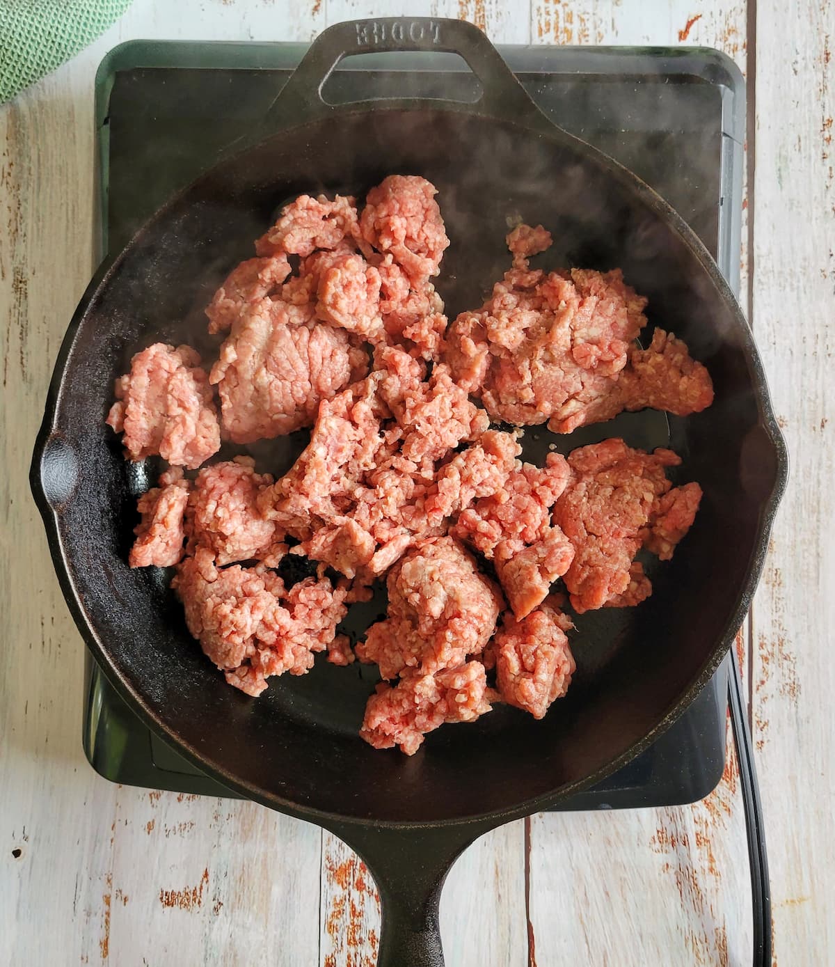 raw ground beef steaming in a cast iron skillet on a burner