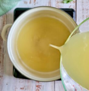 chicken broth being poured into a pot on a burner