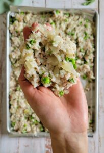 hand holding rice mixed with peas, onions and ground beef over a sheet pan of the rest of the rice mixture