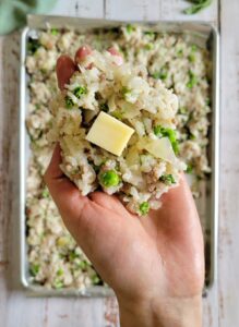 hand holding rice mixed with peas, onions and ground beef with a cube of mozzarella in the middle