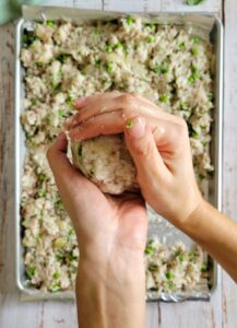 hands forming a rice ball over the sheet pan of the rest of the rice mixture