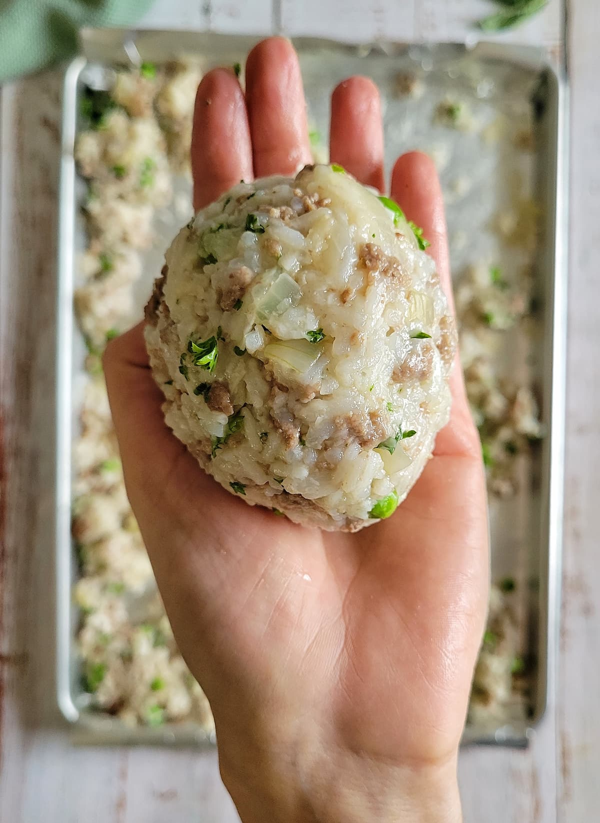 rice ball with peas and ground beef in a hand over a sheet pan of the rice mixture