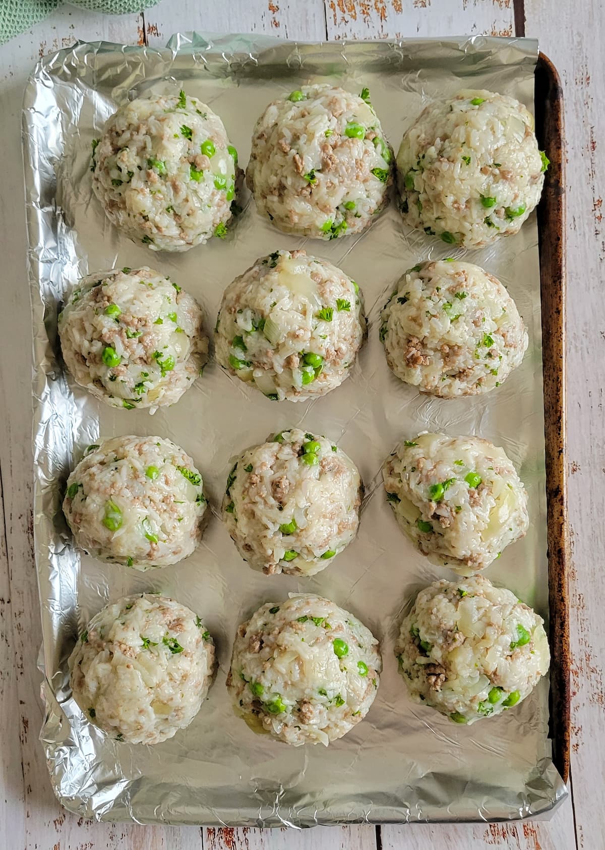 unbreaded rice balls with peas and ground beef on a foil lined baking sheet