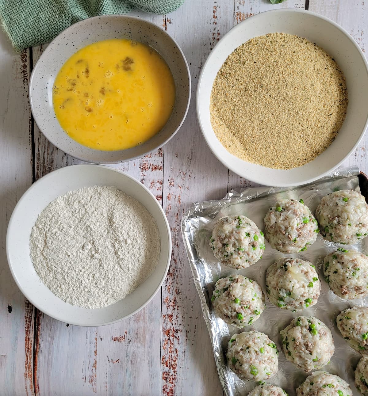3 dredge bowl - 1 flour, 1 egg, 1 breadcrumbs next to a sheet pan with unbreaded rice balls