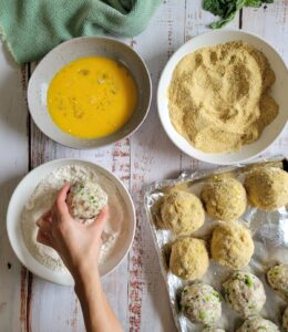 3 dredge bowls - 1 flour, 1 egg, 1 breadcrumbs, hand making rice balls, rolling the ball in the flour mixture, sheet pan of rice balls in frame