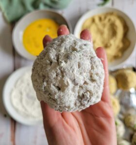 hand holding a floured rice ball over 3 dredge bowls (1 flour, 1 egg, 1 breadcrumbs)