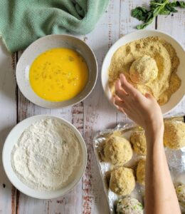 3 dredge bowls - 1 flour, 1 egg, 1 breadcrumbs, hand making rice balls, rolling the ball in the breadcrumb mixture, sheet pan of rice balls in frame