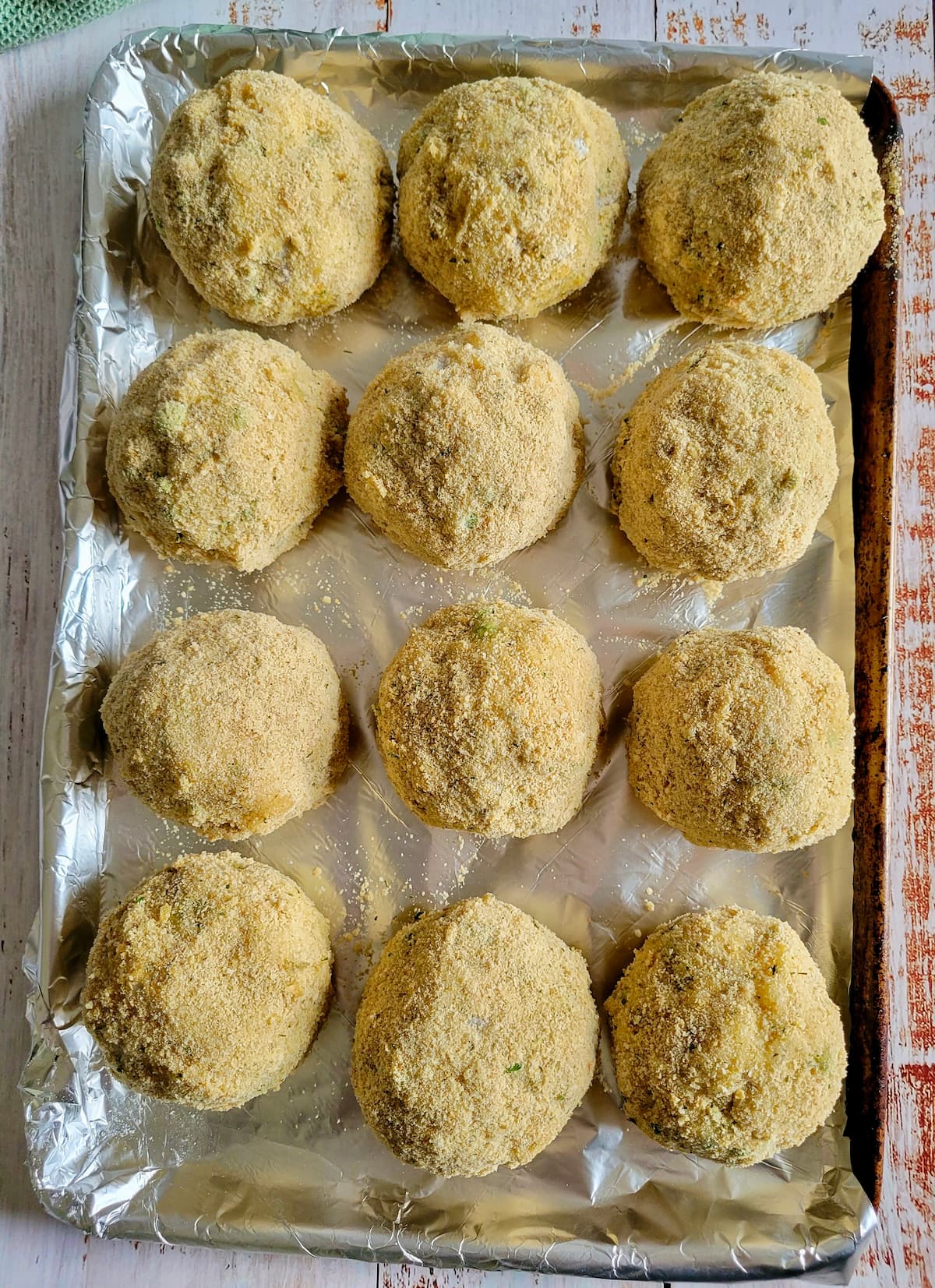 12 breaded uncooked rice balls on a foil lined baking sheet