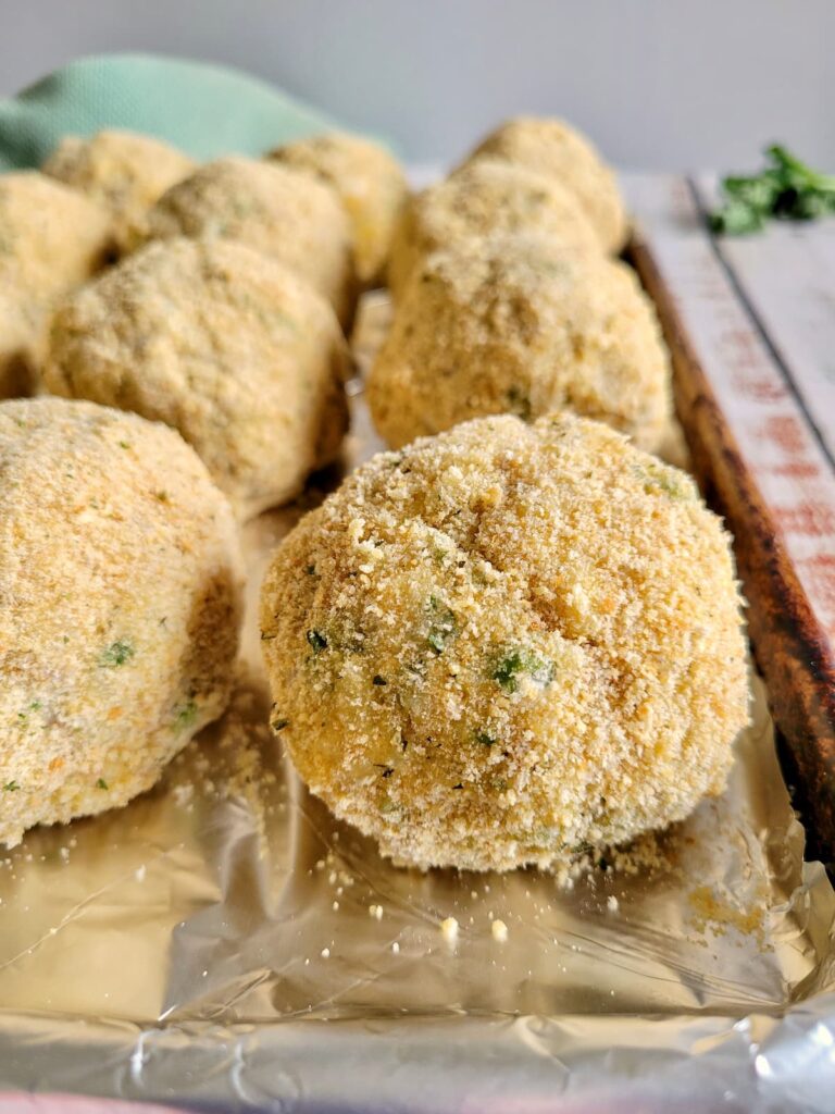 side/front view of breaded uncooked rice balls on a foil lined baking sheet