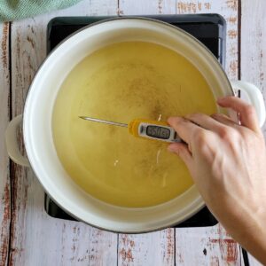 hand with a thermometer reading 350 in a pot of oil on a burner
