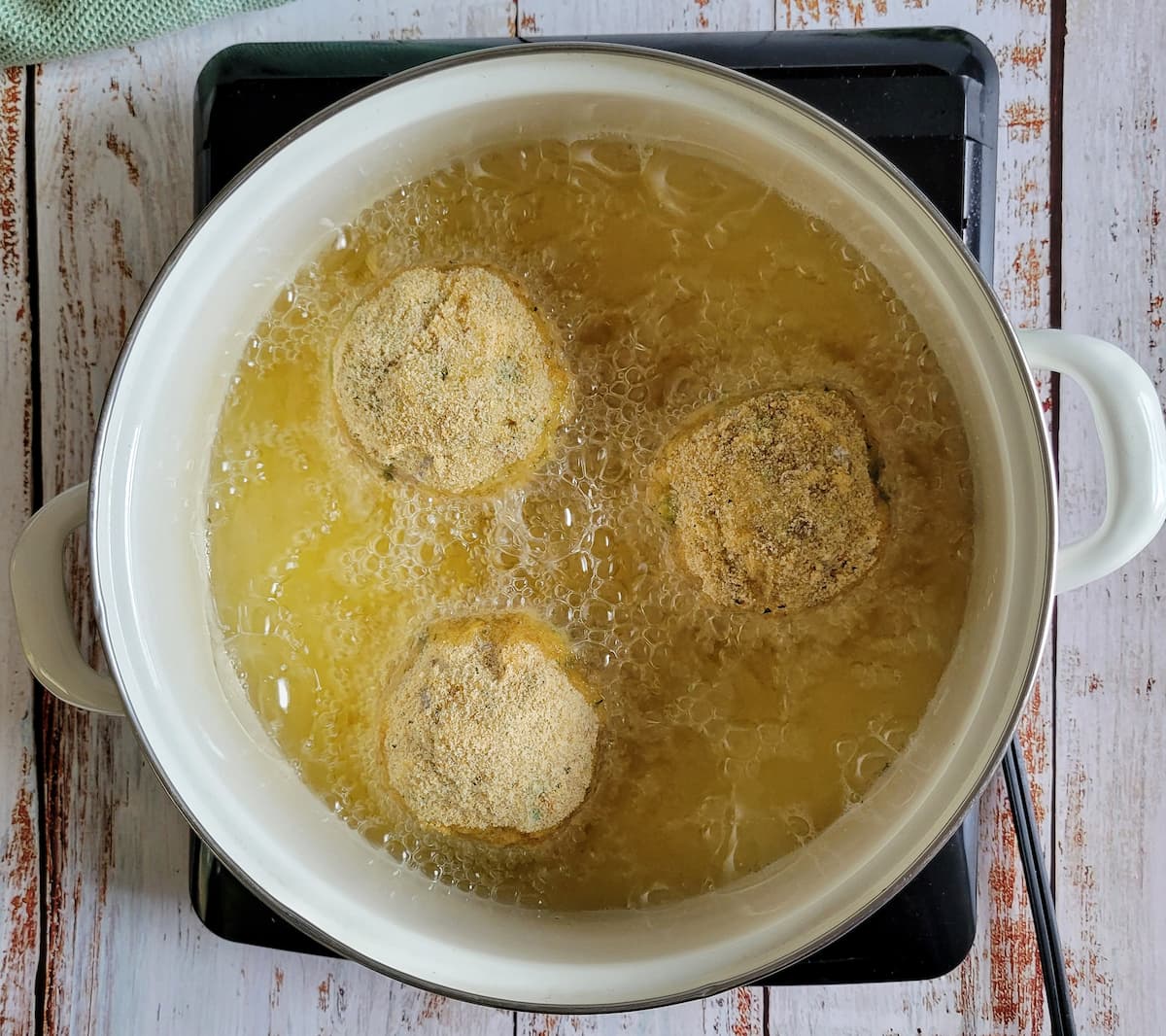 3 breaded rice balls frying in a pot of oil on a burner