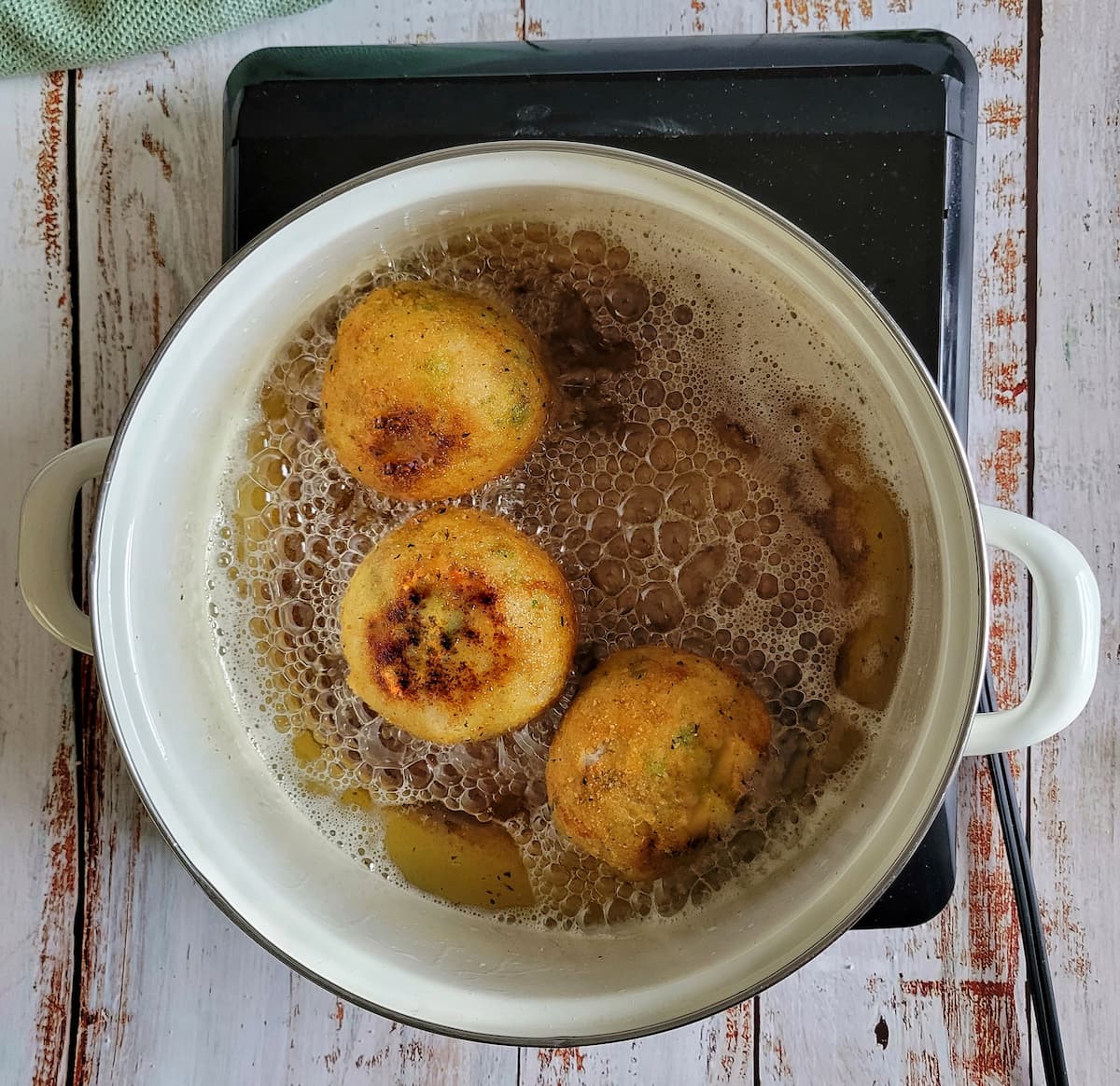 3 crispy rice balls frying in a pot of oil on a burner