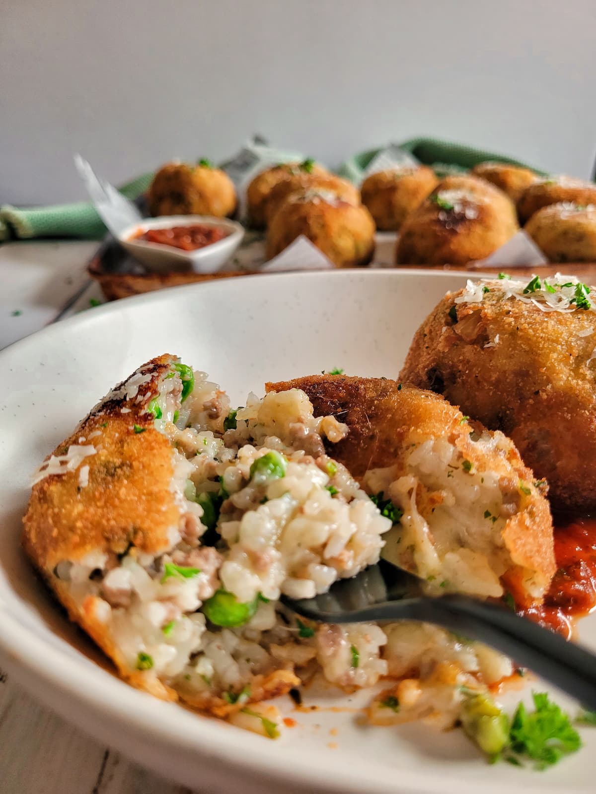 fork in an opened rice ball on a plate next to another one, tray of more in the background with tomato sauce