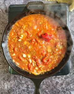 blob of tomato paste in a skillet with tomato sauce, seasonings and diced onions