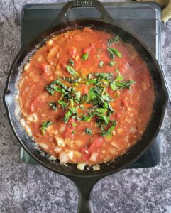 tomato sauce, diced onions and chopped fresh basil in a cast iron skillet on a burner