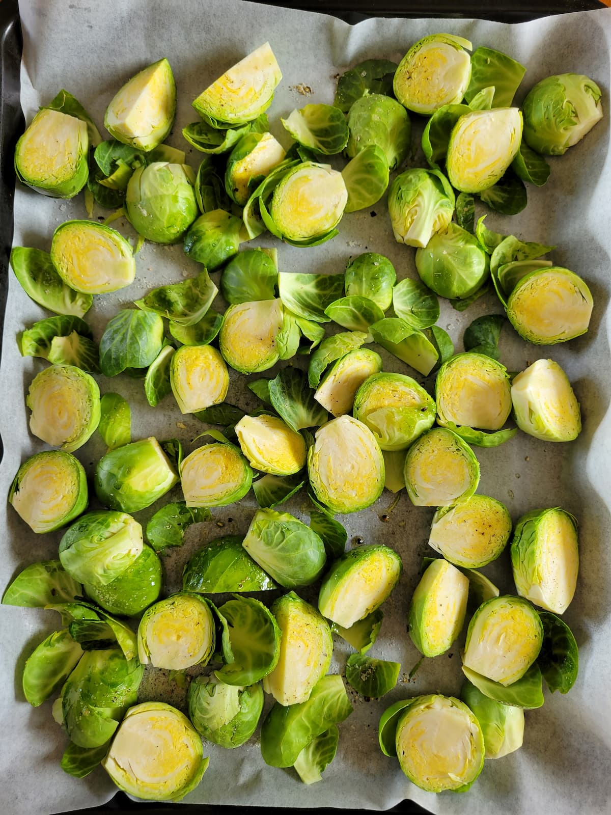 halved raw brussels sprouts with salt, pepper and olive oil spread out onto a parchment lined baking sheet
