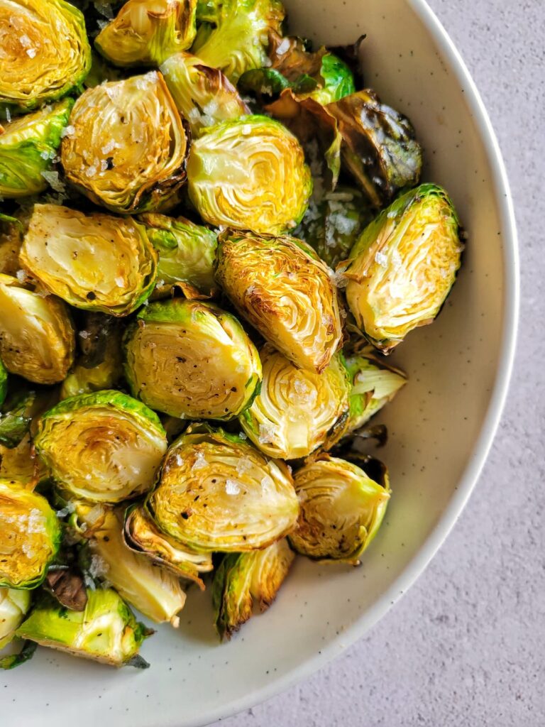 half view of air fried brussels sprouts garnished with flakey sea salt in a bowl