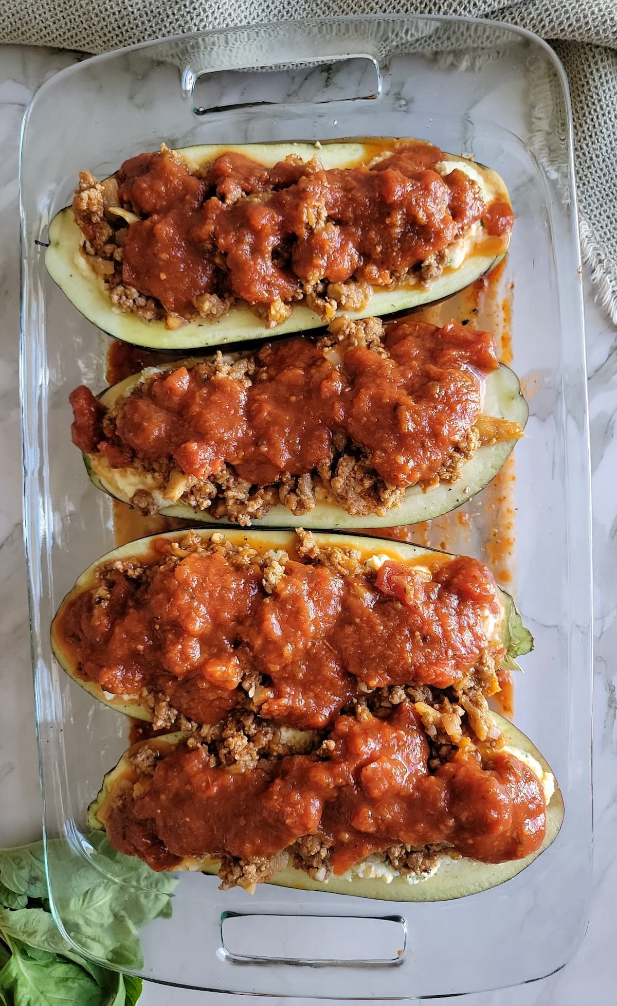 4 eggplant halves filled with tomato sauce and ground beef in a rectangular glass baking dish