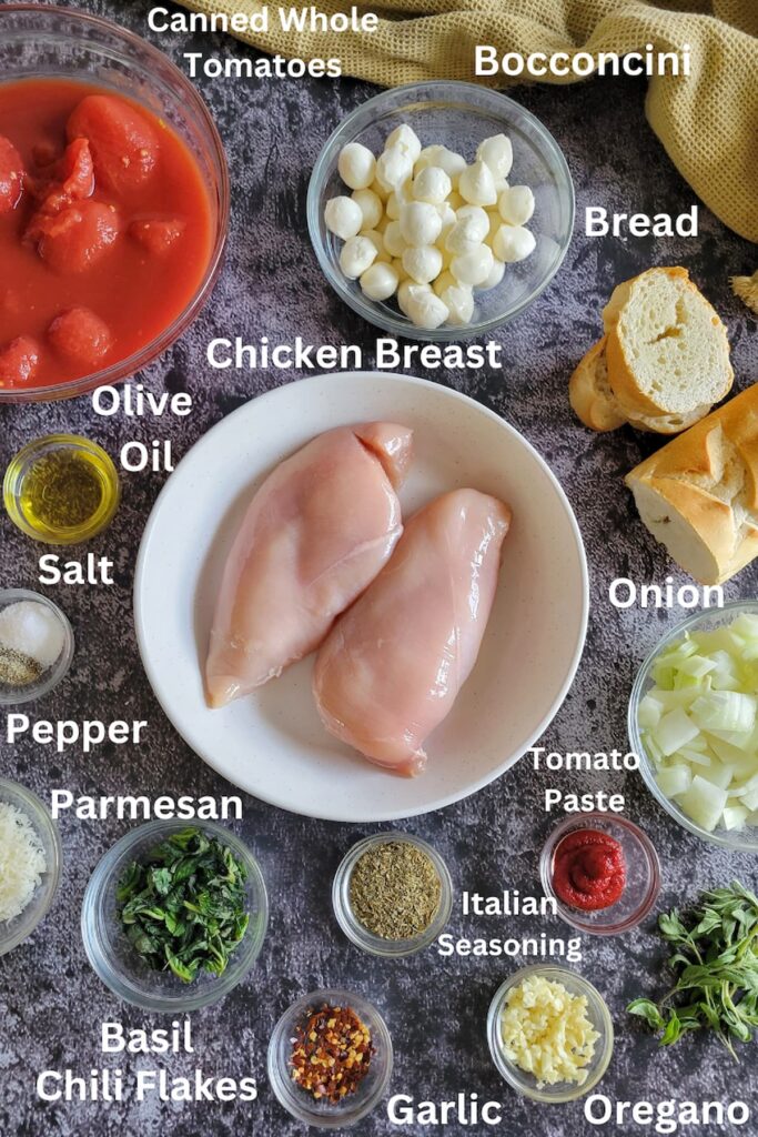 ingredients for cheesy chicken skillet - chicken breasts, bocconcini, whole canned tomatoes, bread, olive oil, salt, pepper, parmesan, basil, chili flakes, italian seasoning, garlic, oregano, tomato paste, onion