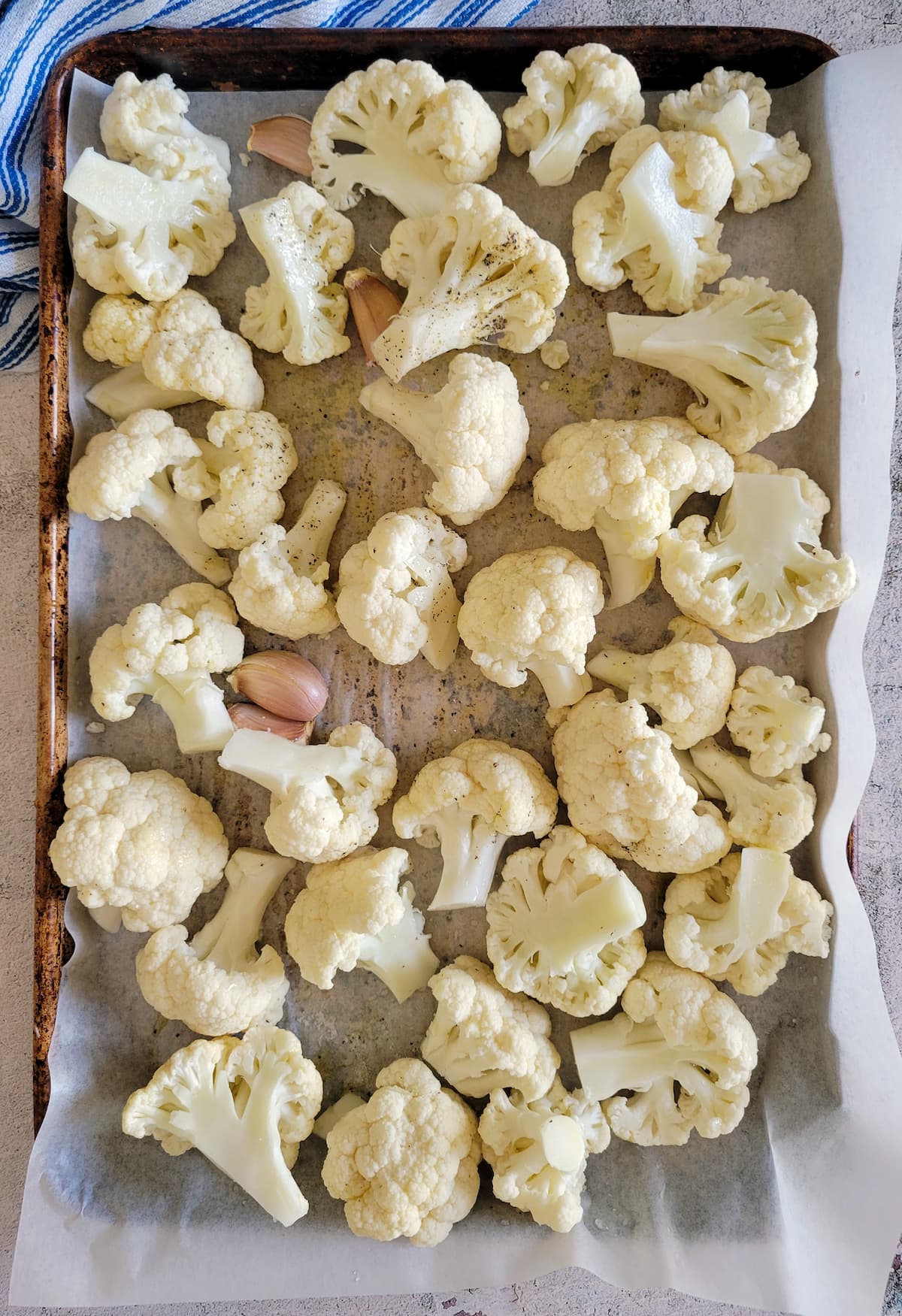 raw cauliflower and unpeeled garlic cloves on a parchment lined sheet pan