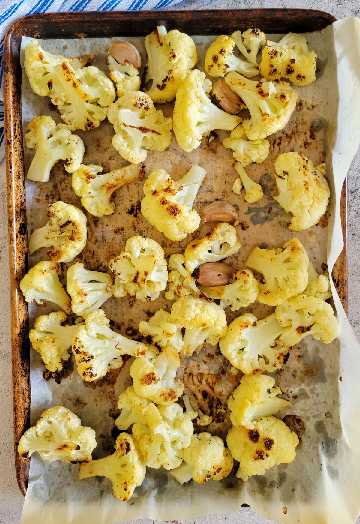 roasted cauliflower and unpeeled garlic cloves on a parchment lined sheet pan