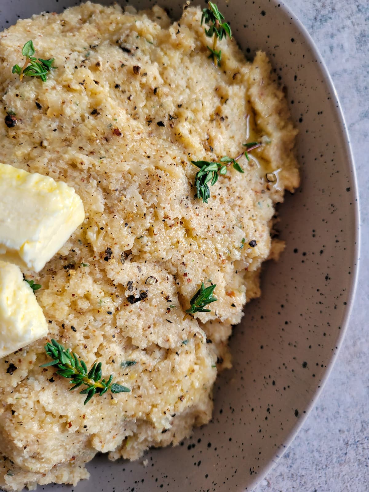 cauliflower mashed potatoes in a bowl topped with butter and fresh thyme