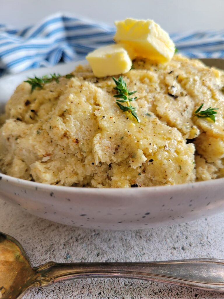 cauliflower mashed potatoes in a bowl topped with butter and fresh thyme