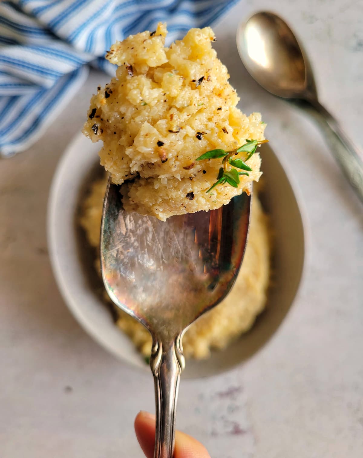 spoon with some mashed cauliflower on it garnished with fresh cracked pepper and thyme