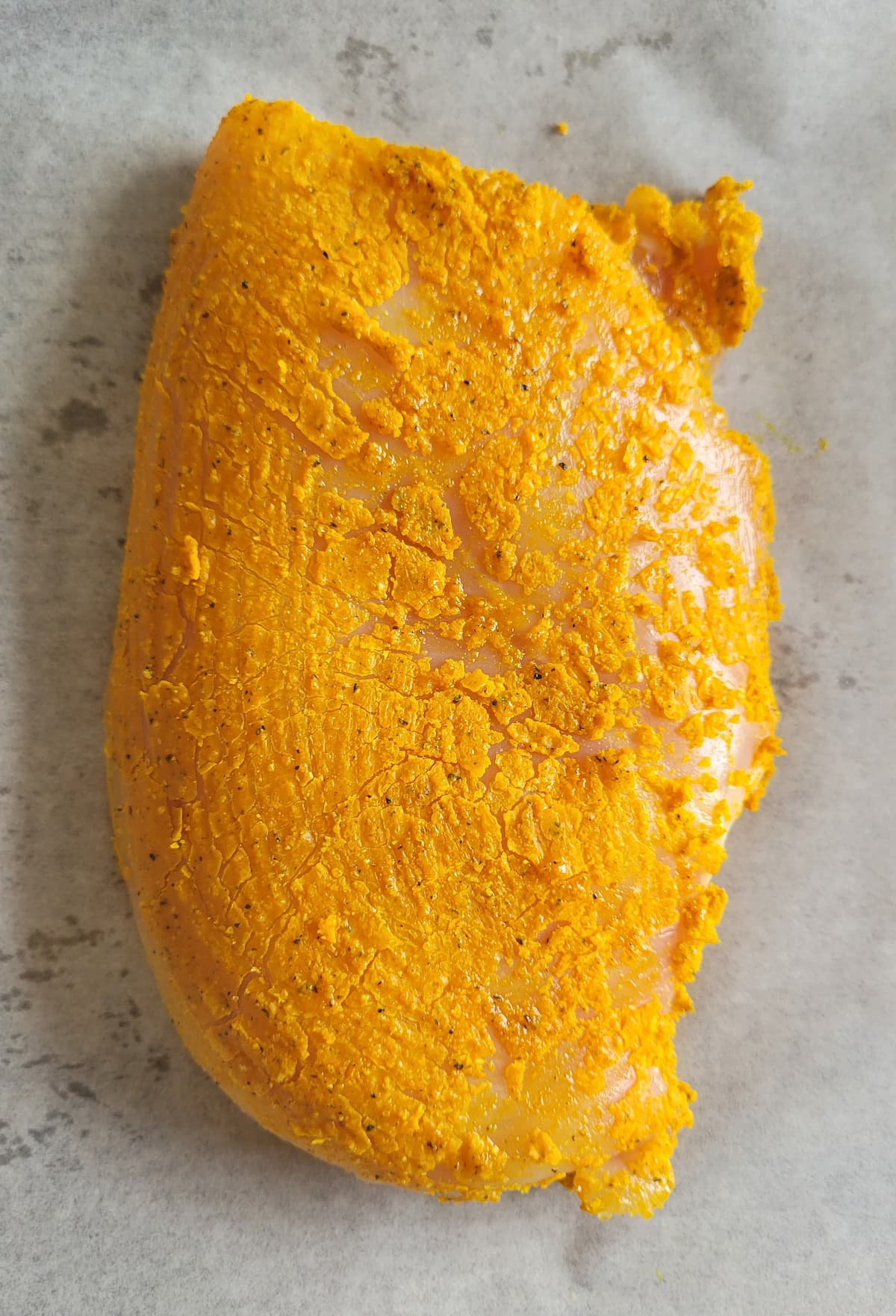 raw chicken breast with a bright yellow crust