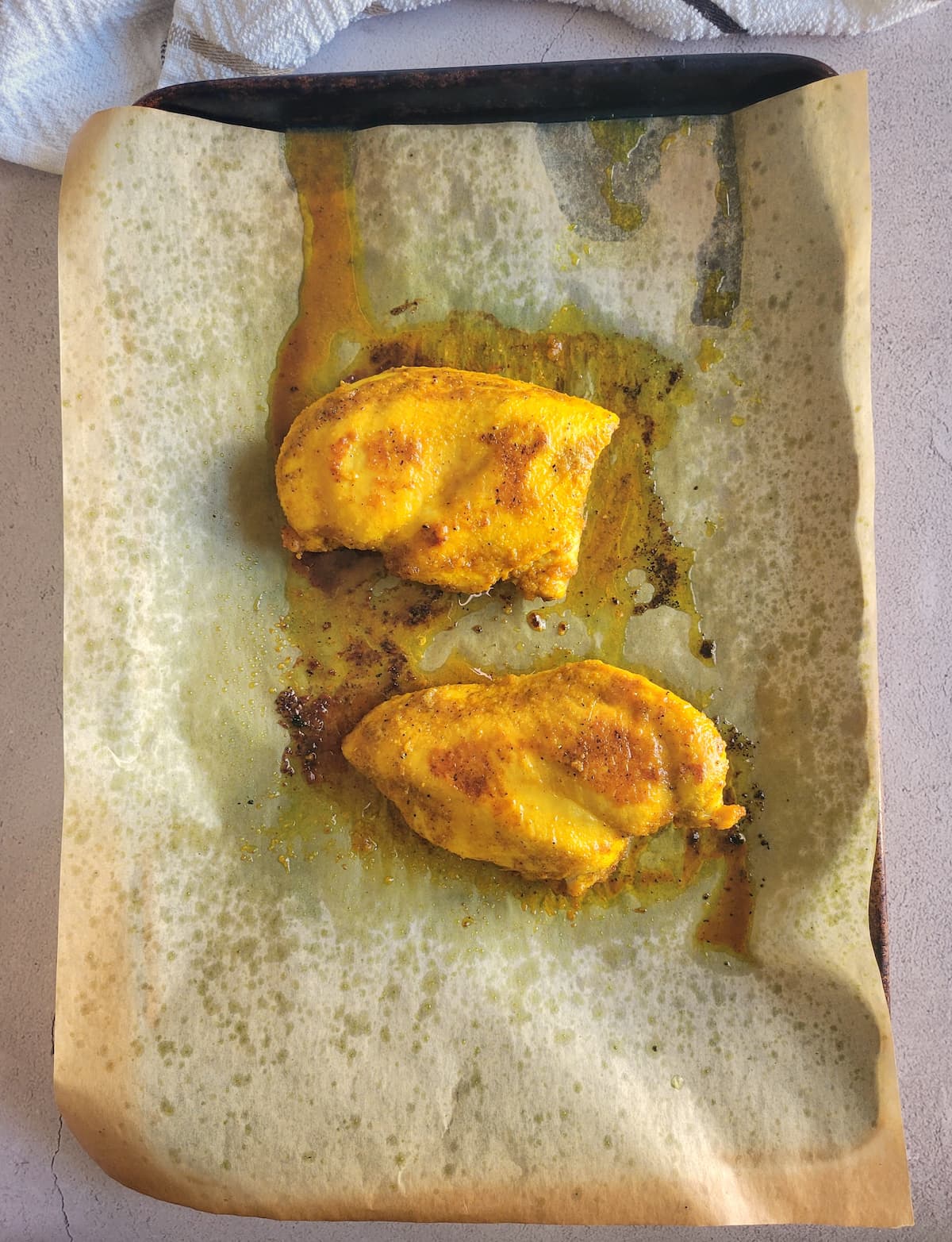 two cooked yellow chicken breasts on a parchment lined baking sheet