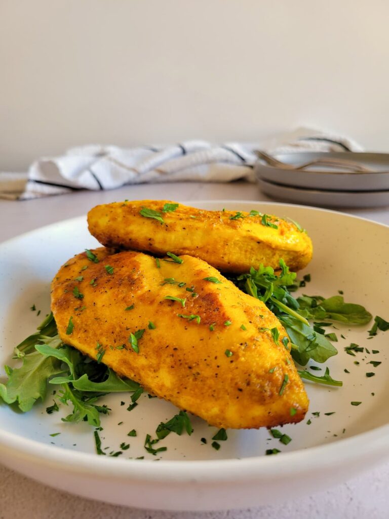 two turmeric chicken breasts on a bed of arugula on a plate garnished with fresh chopped parsley