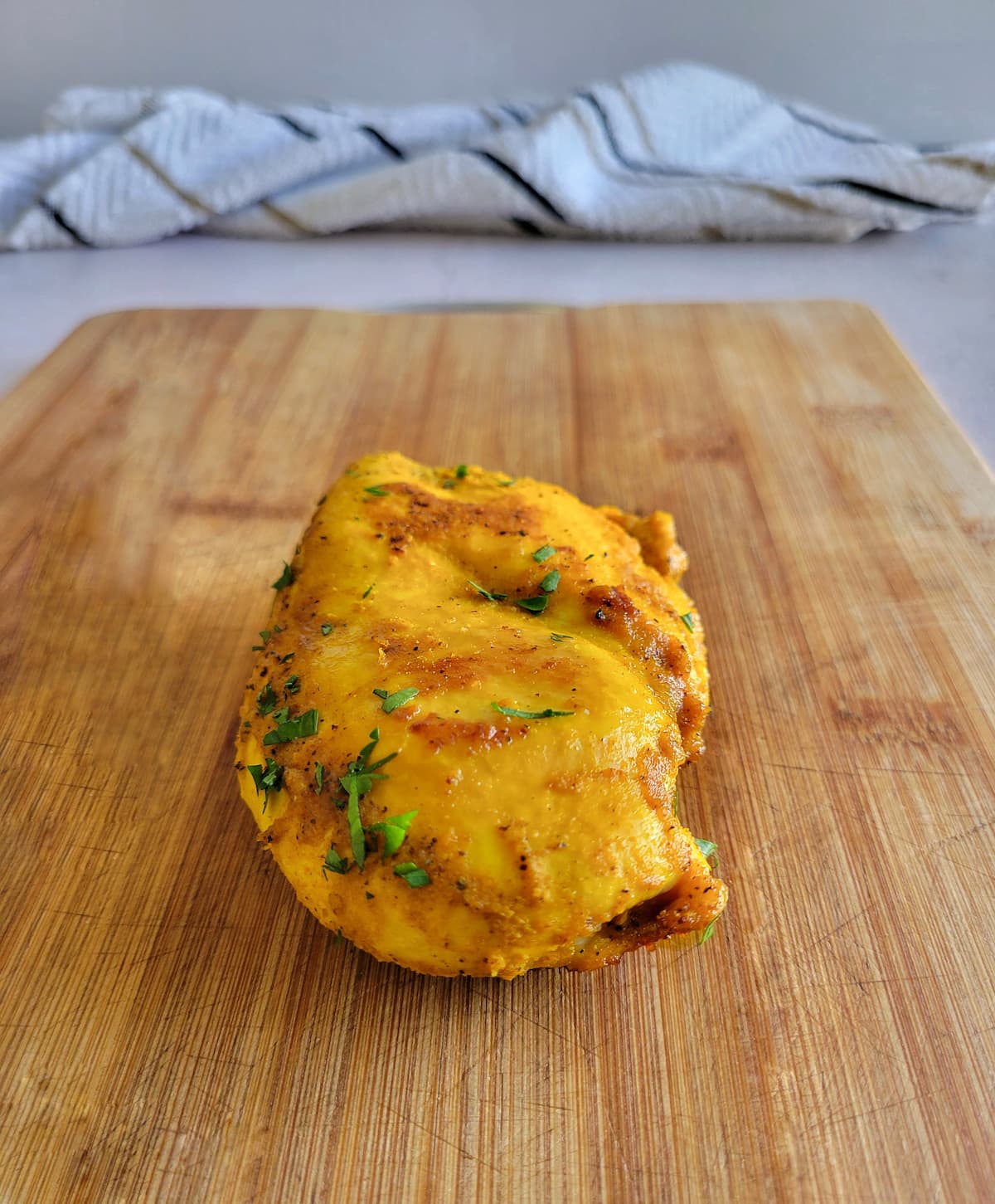 turmeric chicken breast on a cutting board garnished with fresh chopped parsley