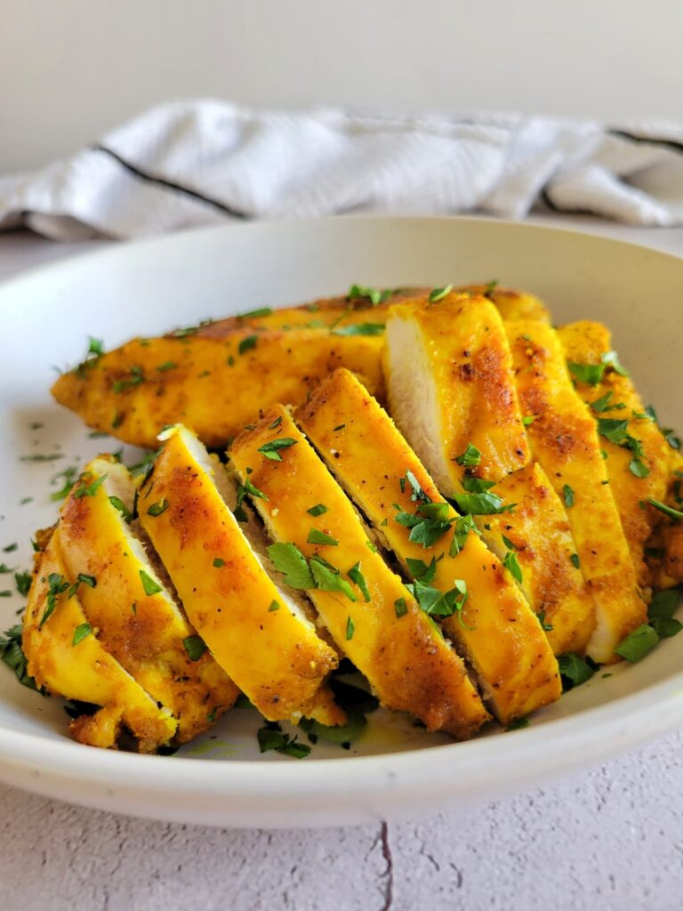 sliced yellow chicken breast in a bowl garnished with fresh chopped parsley