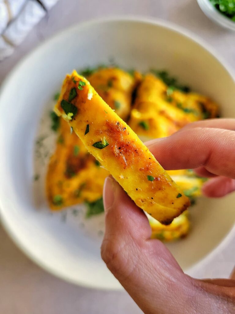 hand holding a slice of turmeric chicken up to the camera over a bowl with the rest of it
