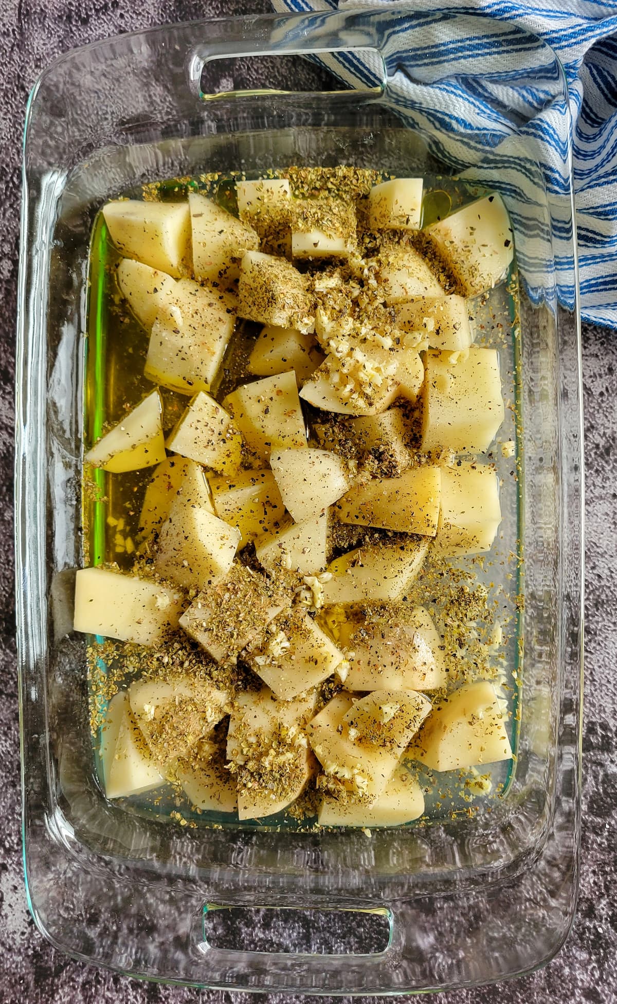 raw potato chunks in a casserole dish with minced garlic, oregano, olive oil and water