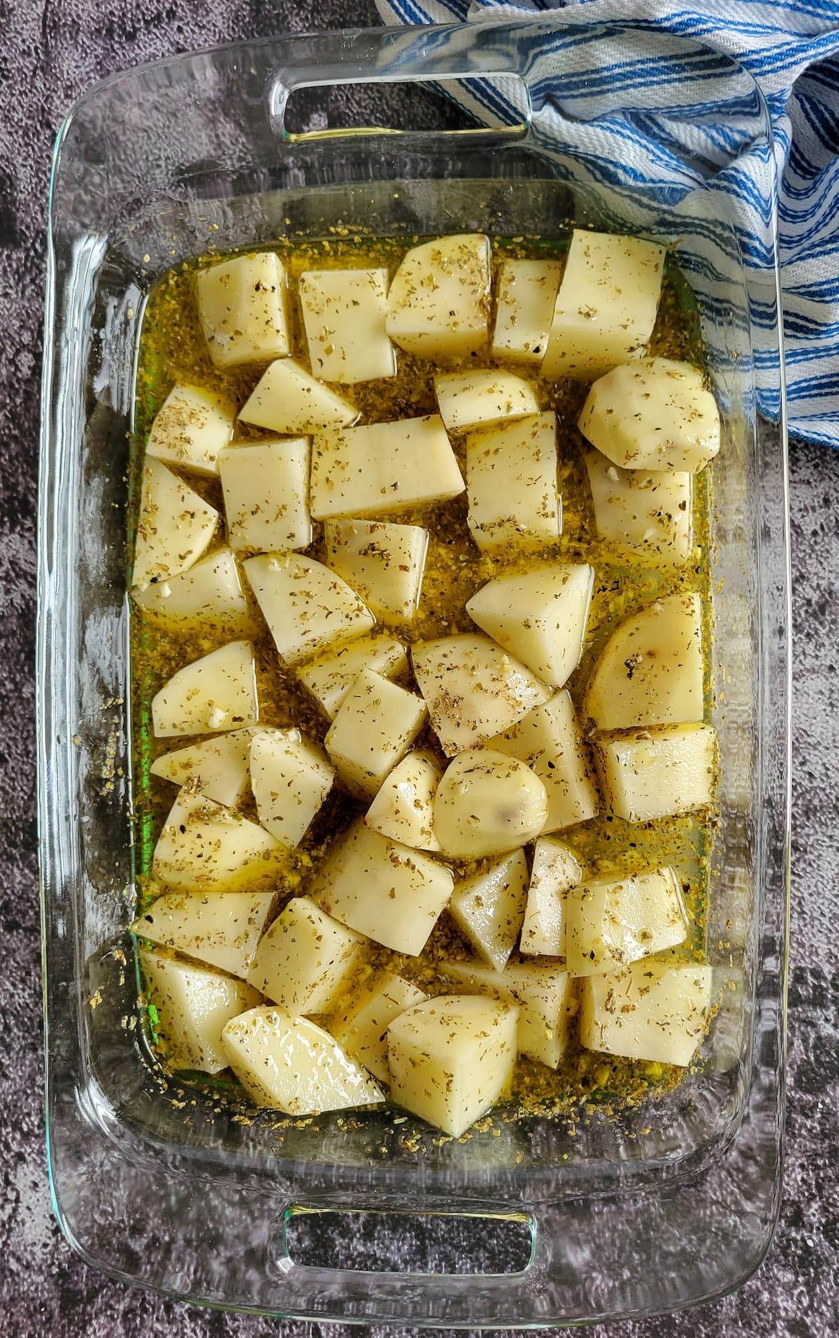 raw seasoned potato chunks in olive oil in a casserole dish