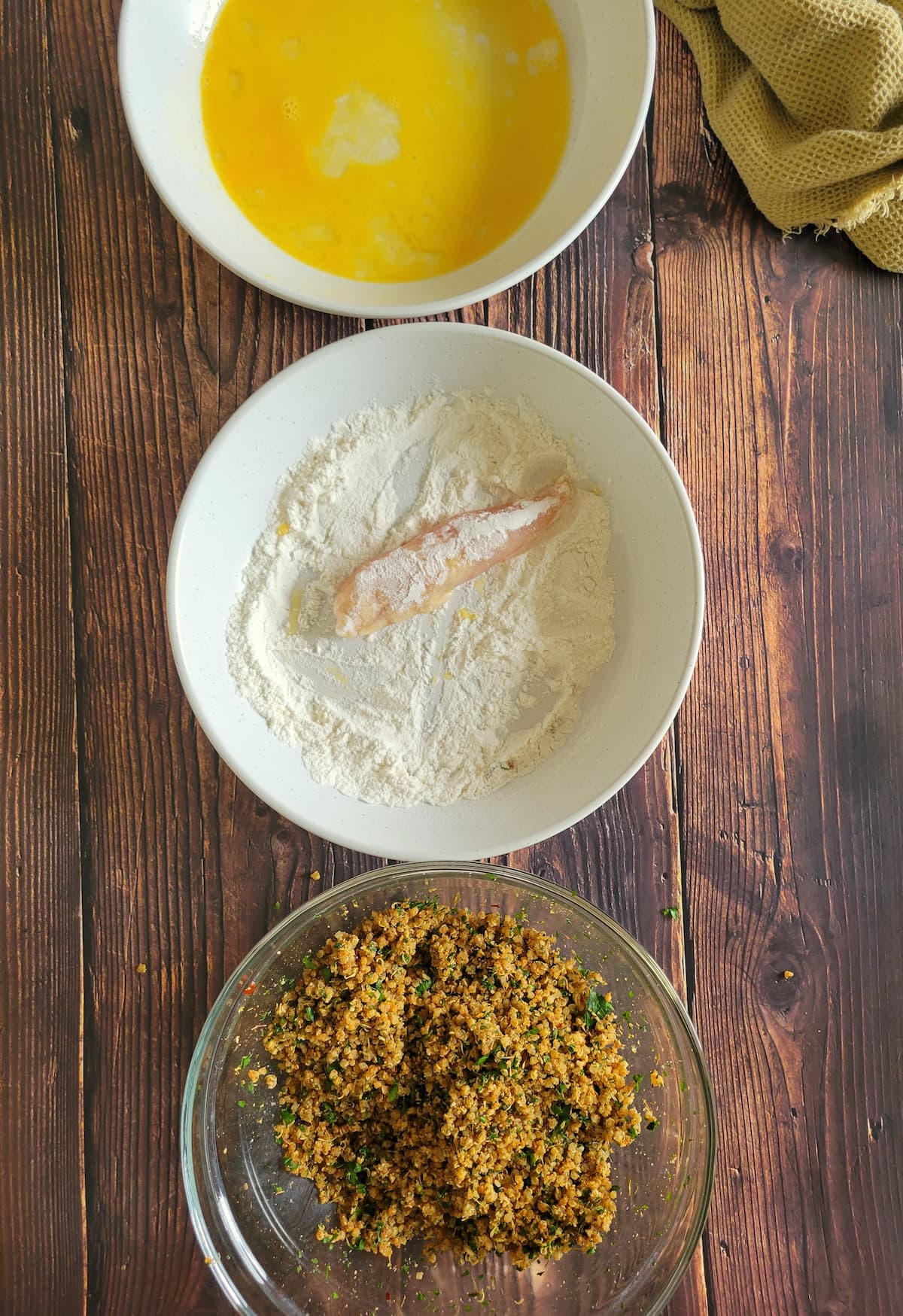 3 bowls - one of beaten egg, one of flour and one of a quinoa coating mixture, chicken tender in the bowl of flour