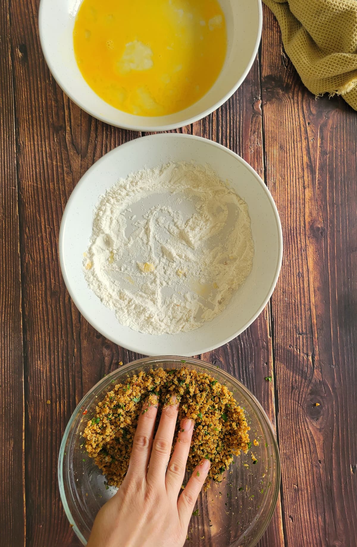 three bowls - one of beaten egg, one of flour and one with a hand in a quinoa coating mixture