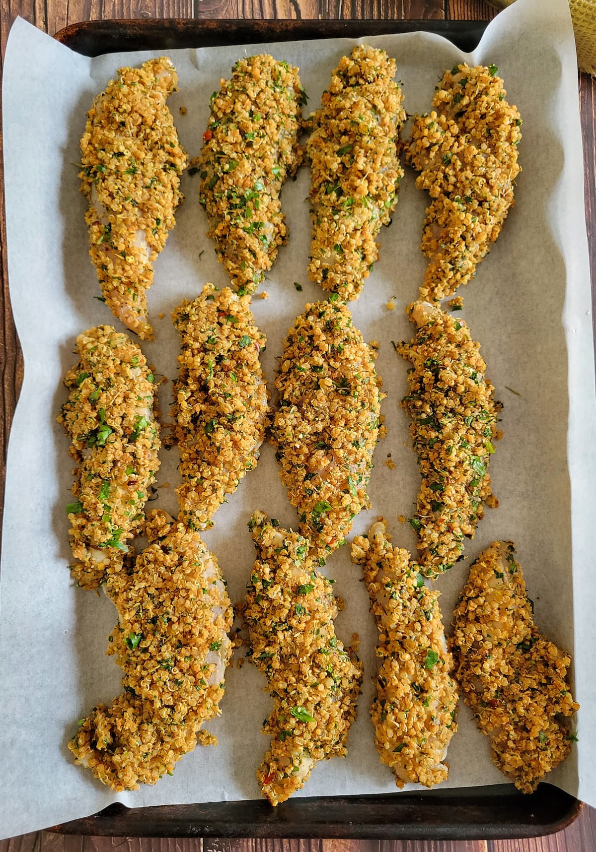 uncooked quinoa coated chicken tenders on a parchment lined baking sheet