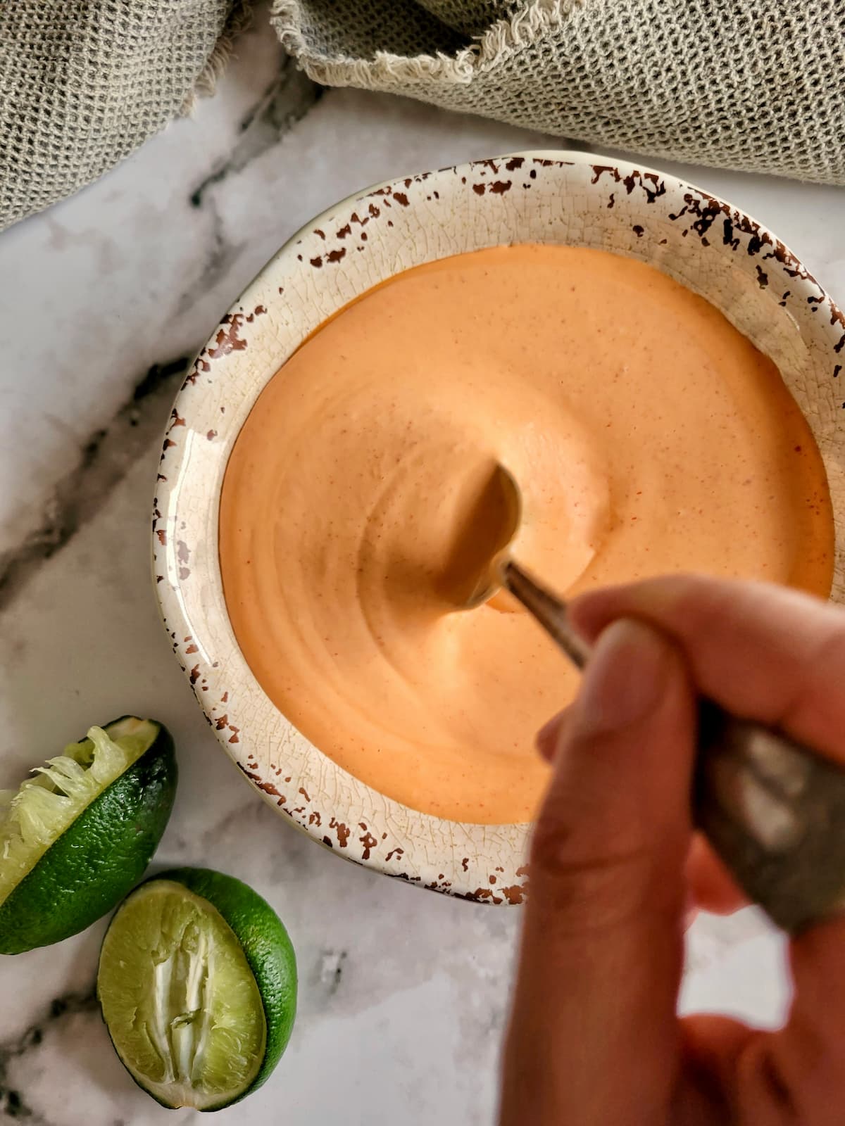 hand stirring an orange sauce in a bowl, limes in the background