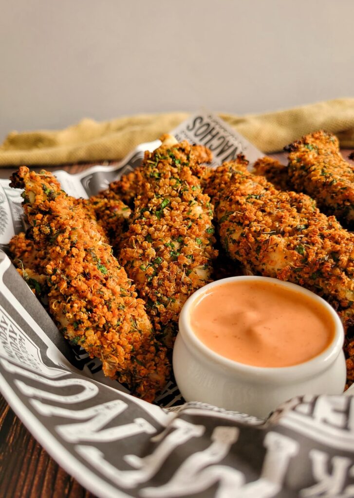 quinoa coated chicken tenders in a lined basket with an orange dipping sauce