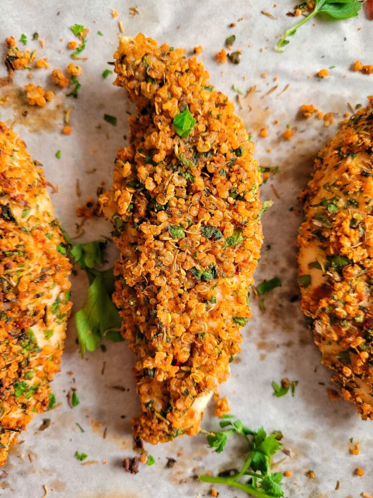 quinoa coated chicken tenders on parchment garnished with fresh parsley