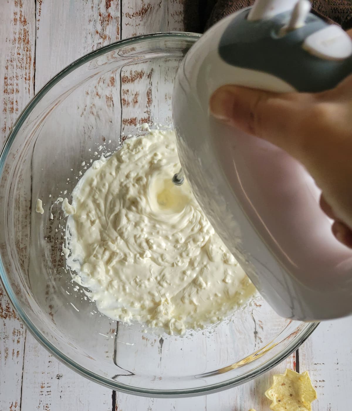 hand with electric mixer beating sour cream and cream cheese in a bowl