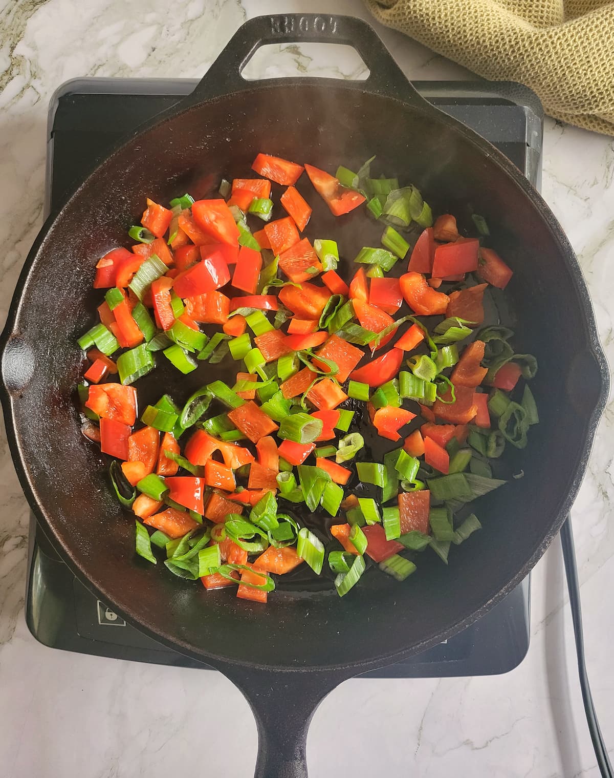 chopped green onions and red peppers in a cast iron skillet on a burner