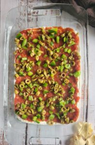 diced green peppers and green olives on top of a layer of salsa and sour cream in a rectangular glass baking dish