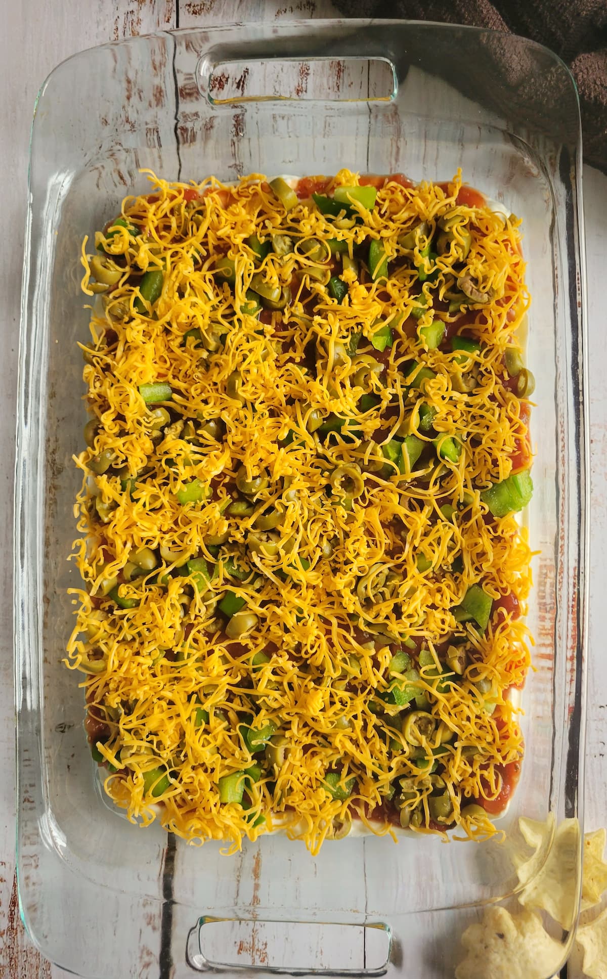 nacho dip topped with shredded cheddar cheese layered in a rectangular baking dish