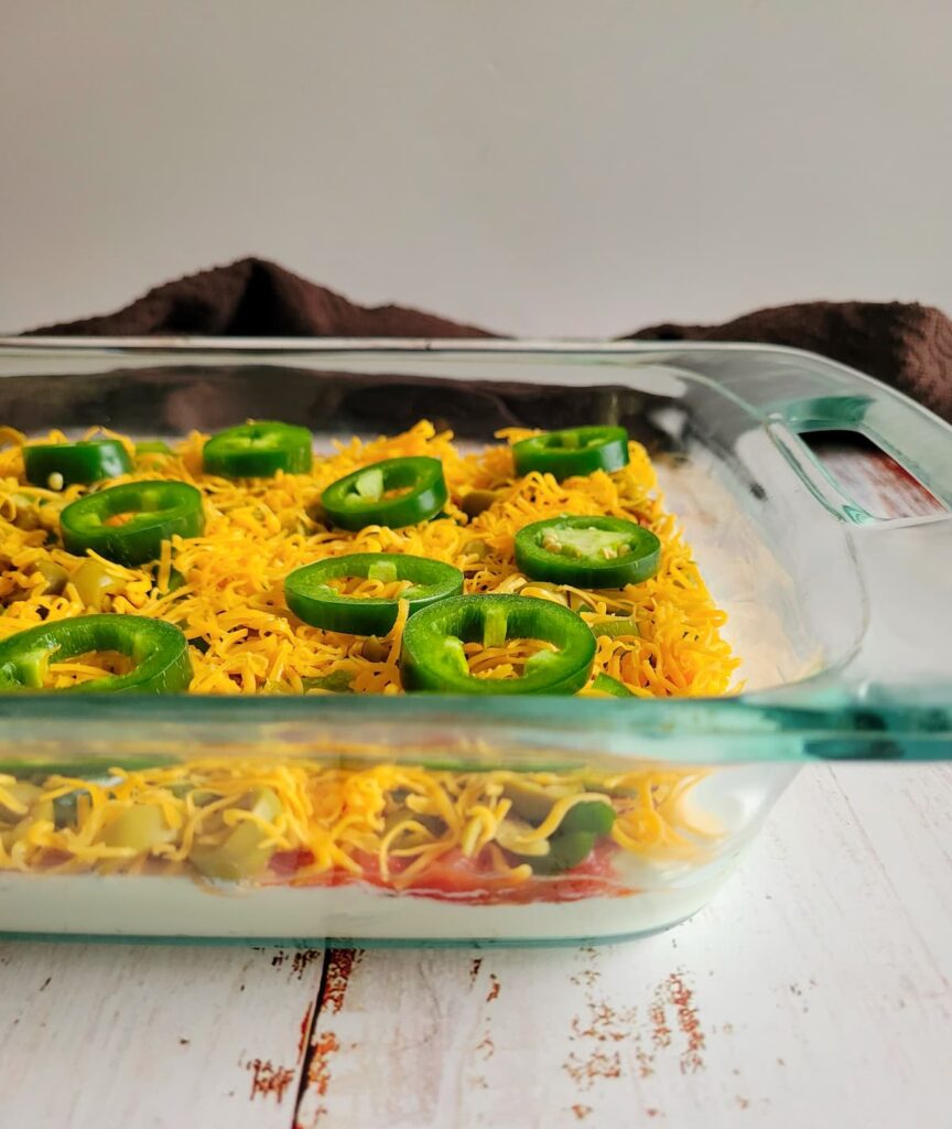 side view of layered nacho dip topped with shredded cheddar cheese and sliced jalapenos