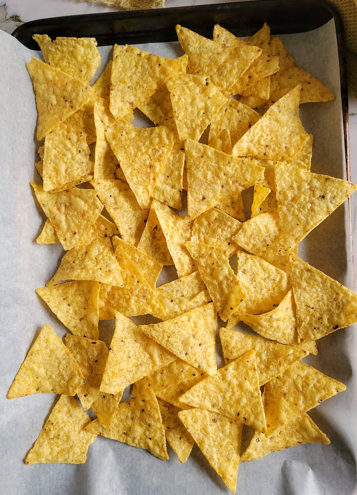 tortilla chips spread out on a parchment lined baking sheet