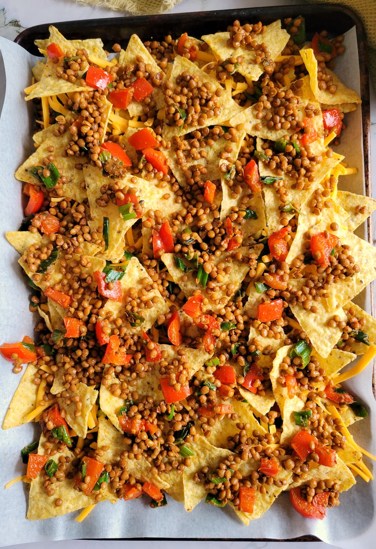 sheet pan with tortilla chips topped with lentils, red peppers and green onions