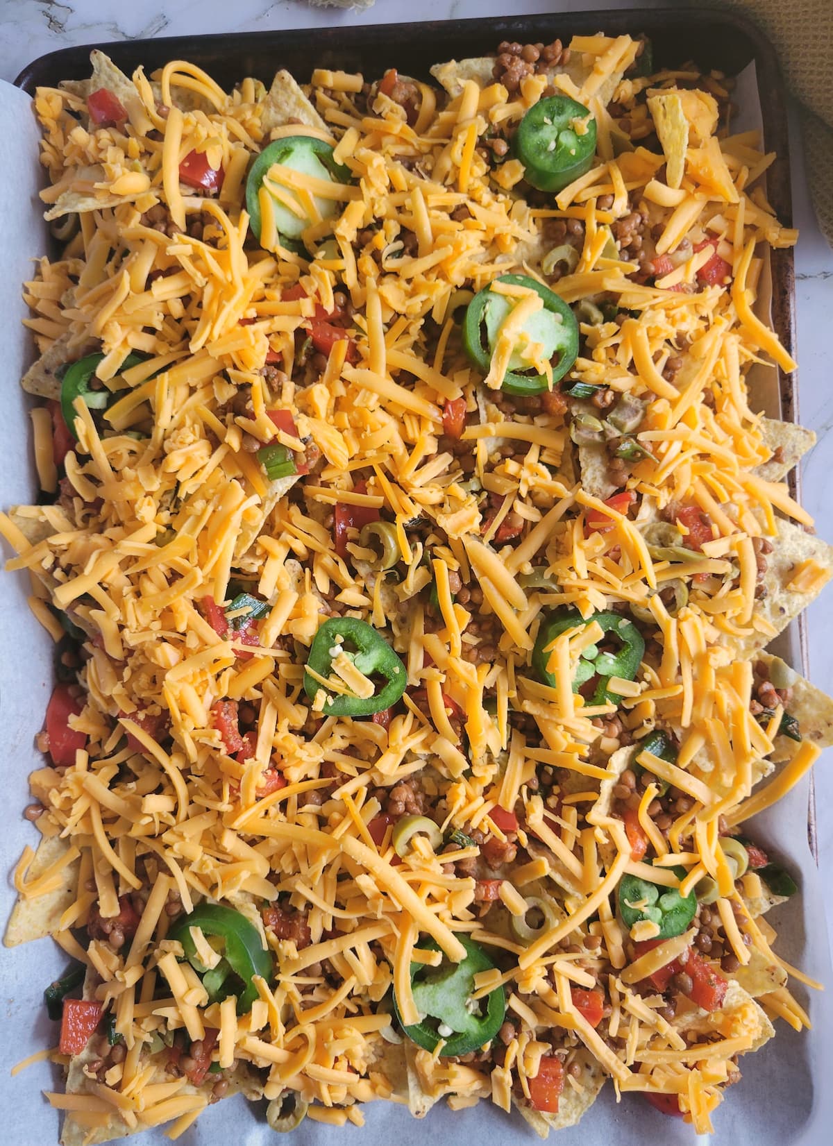 sheet pan of loaded nachos with sliced jalapenos and unmelted cheddar cheese